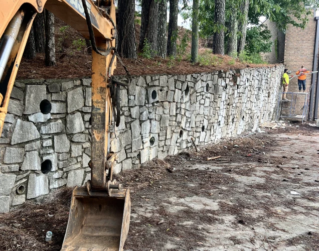 excavator and two engineers analyzing how to repair a 10 foot tall retaining wall